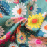 Sage green twill cotton fabric with the Blazing print featuring oversized daisy blooms in coral, pink, yellow and orange, with teal and navy polka-dot circles, shown draped and gathered.