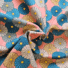 Pink twill cotton fabric with the Flowerella retro daisy print featuring large blooms in teal, dusky blue, mustard and grey with yellow centres, shown draped and gathered.