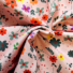 Twill cotton fabric in pink with a floral print of orange, purple, and grey flowers with green foliage.