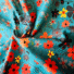 Twill cotton fabric in turquoise with a floral print of orange, grey, and yellow flowers with foliage.