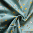 Powder blue twill cotton fabric with a floral print featuring yellow sunflowers, white daisies, small orange flowers, green leafy sprigs and butterflies, shown draped and gathered.
