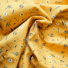 Yellow twill cotton fabric with a floral print featuring white daisies, small orange flowers and blue-grey leafy sprigs, shown draped and gathered.