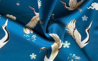 Viscose heavenly wings sea blue. Sea blue fabric with white storks flying among small multi-coloured flowers
