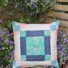 Valley Falls Quilt Block on a garden bench among small purple flowers. Pastel colours on the outside. Floral pattern inside.