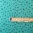 Little Rose cotton fabric in Morning Green, featuring small clustered sprigs of red and cream rosebuds with green leaves scattered on a teal background, with a fine dotted pattern. With ruler to show size of design