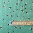 Bee World (sea foam) cotton fabric featuring a scattered pattern of illustrated bumblebees in black, yellow, and white on a green background. With ruler to show size of design.